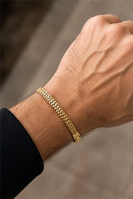 Masculine man's wrist wearing a single gold mesh bracelet as a simple affordable jewelry upgrade.