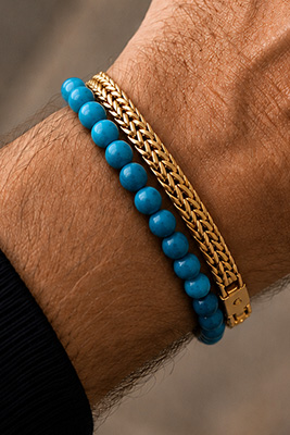 Blue bead bracelet paired with a gold mesh bracelet on a masculine wrist.