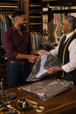 A satisfied customer speaking warmly with his tailor while collecting several professionally altered garments