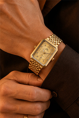 Well-dressed man wearing a sophisticated $25 gold-tone watch with a rectangular case, pale textured face, and gold bracelet.