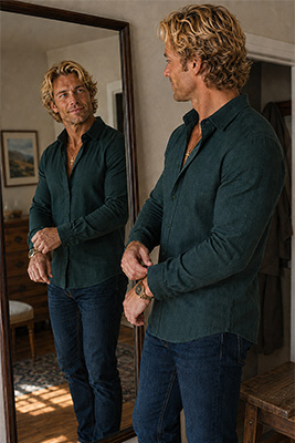 A man approving the perfect fit of a richly textured, classic men's shirt in a full-length mirror
