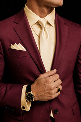 Elegant wedding guest wearing a burgundy suit with tasteful gold watch, black onyx ring, cuff links, and subtle chain.