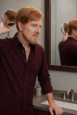 Mature man using two mirrors to inspect the back of his neck, ears, and scalp under good light