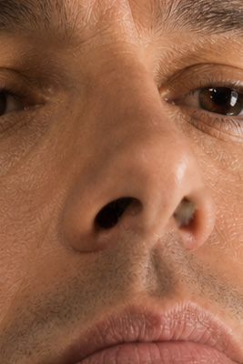 Man looking in bathroom mirror with a visible booger in one nostril