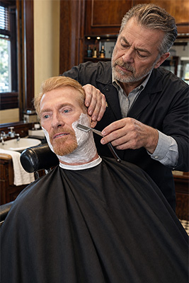 Experienced barber giving a mature man a traditional straight-razor shave with rich shaving-soap lather